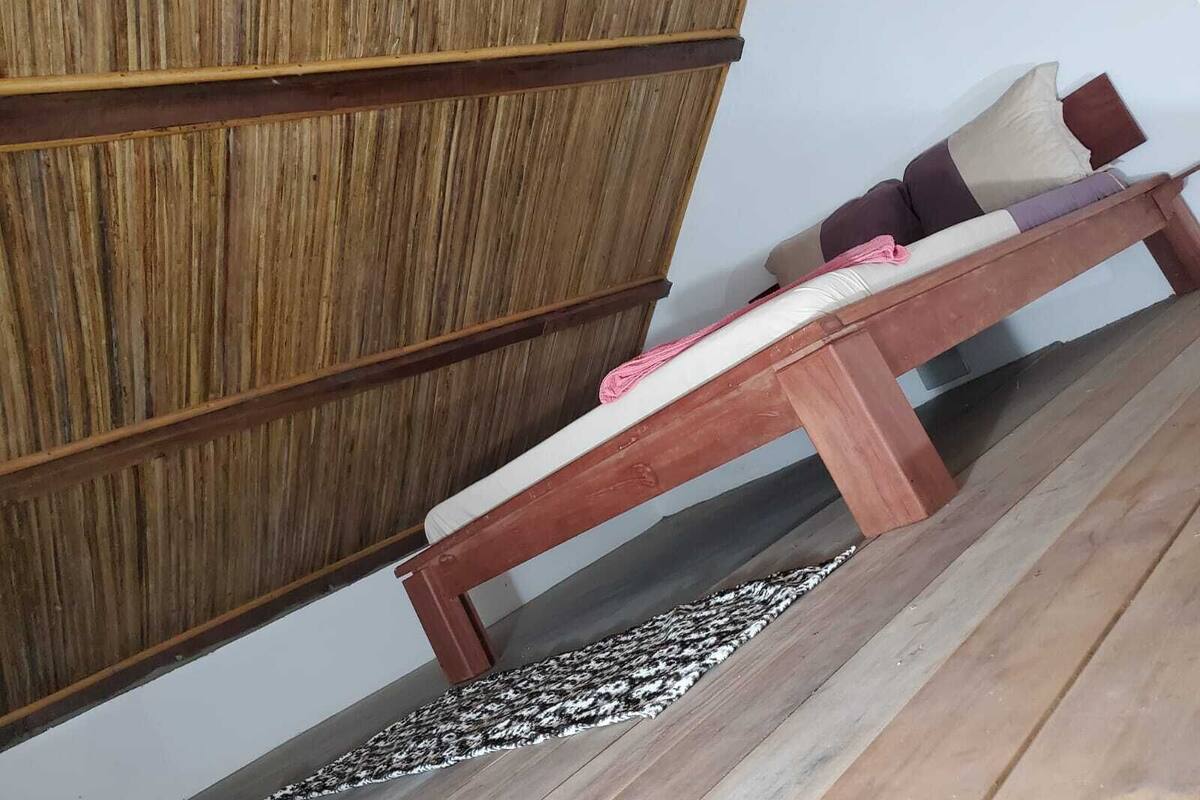 Un banco de madera con cojines, un muro de fondo, un tapete estampado en el suelo y un aparador de madera.