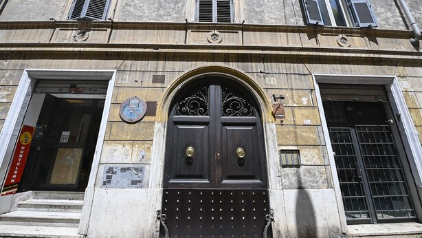 Un bâtiment doté d’une grande entrée en arc de cercle, d’une porte noire ornée d’une poignée décorative et d’une plaque placée au-dessus de la porte.