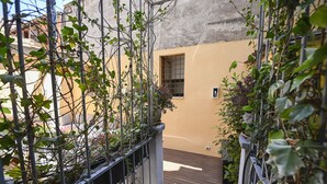 Un étroit couloir extérieur, avec une clôture métallique d’un côté et un mur jaune de l’autre.