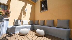 Un espace extérieur lumineux, aménagé avec un canapé et des poufs, une petite fenêtre et une plante en pot.