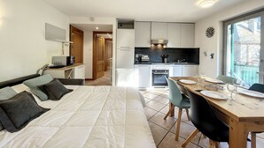 A modern hotel room with a bed, a dining table set for two, a kitchen area, and a view of the outside. - Apartment in central Chamonix - 6 people, parking, 3-star comfort (Chamonix-Mont-Blanc)