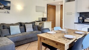 A modern living room with a grey sofa, a wooden dining table set for two, and a kitchen area with white cabinets and appliances. - Apartment in central Chamonix - 6 people, parking, 3-star comfort (Chamonix-Mont-Blanc)