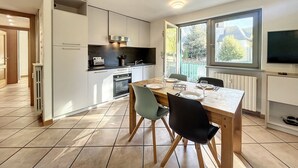 A modern kitchen with white cabinets, a dining table set for four, and a TV mounted on the wall. - Apartment in central Chamonix - 6 people, parking, 3-star comfort (Chamonix-Mont-Blanc)