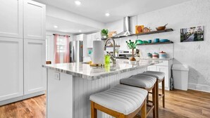 Una cocina moderna con armarios blancos, una isla de mármol con taburetes y una campana de acero inoxidable.