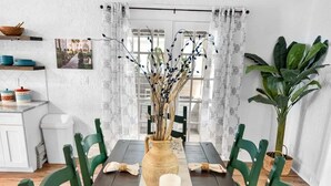 Un comedor con una mesa de madera oscura, sillas verdes, un jarrón central con ramas y un camino de mesa estampado.