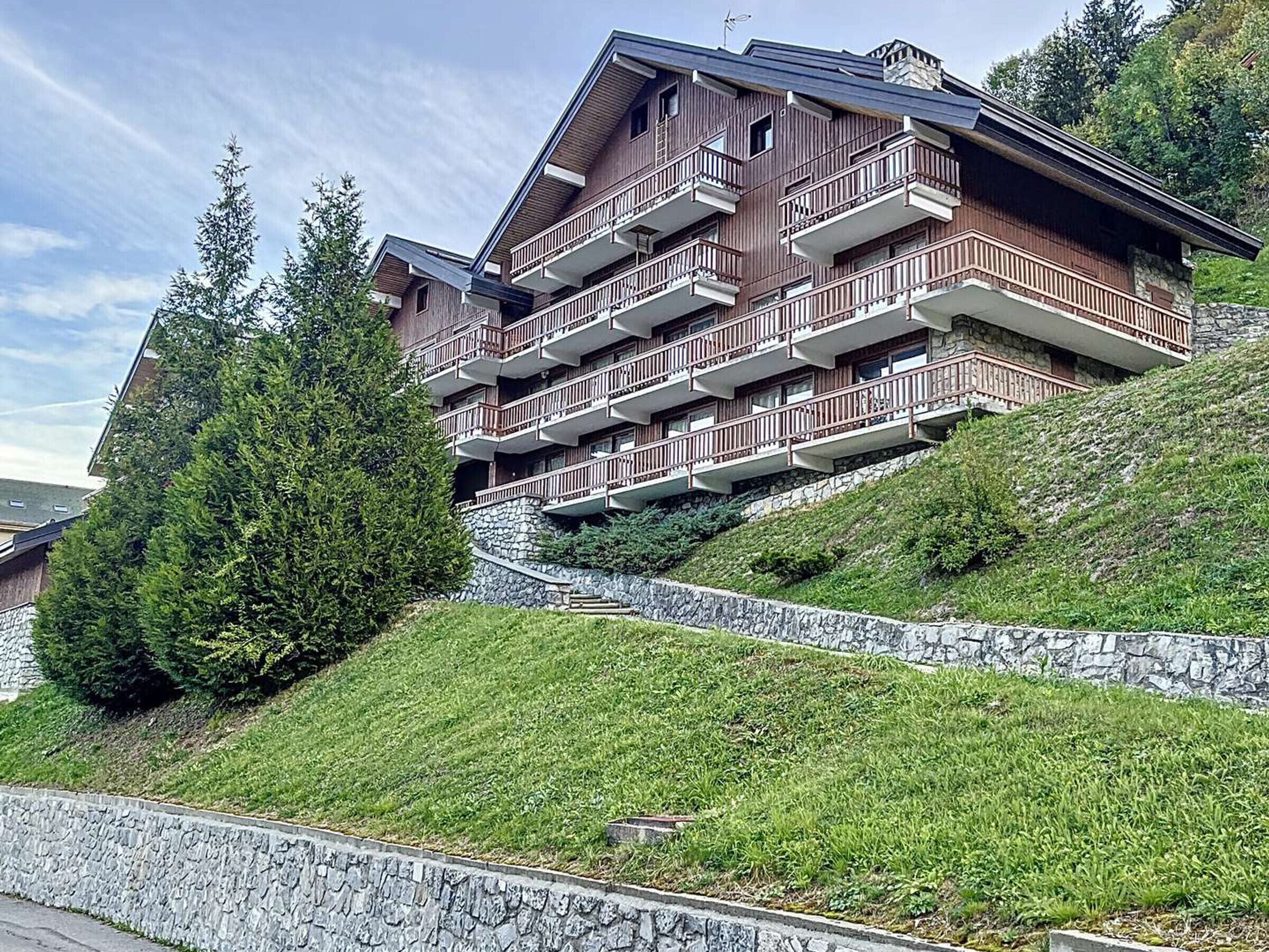 Un hôtel à plusieurs étages, doté de balcons, situé sur une colline, avec un mur de soutènement en pierre et de la végétation.