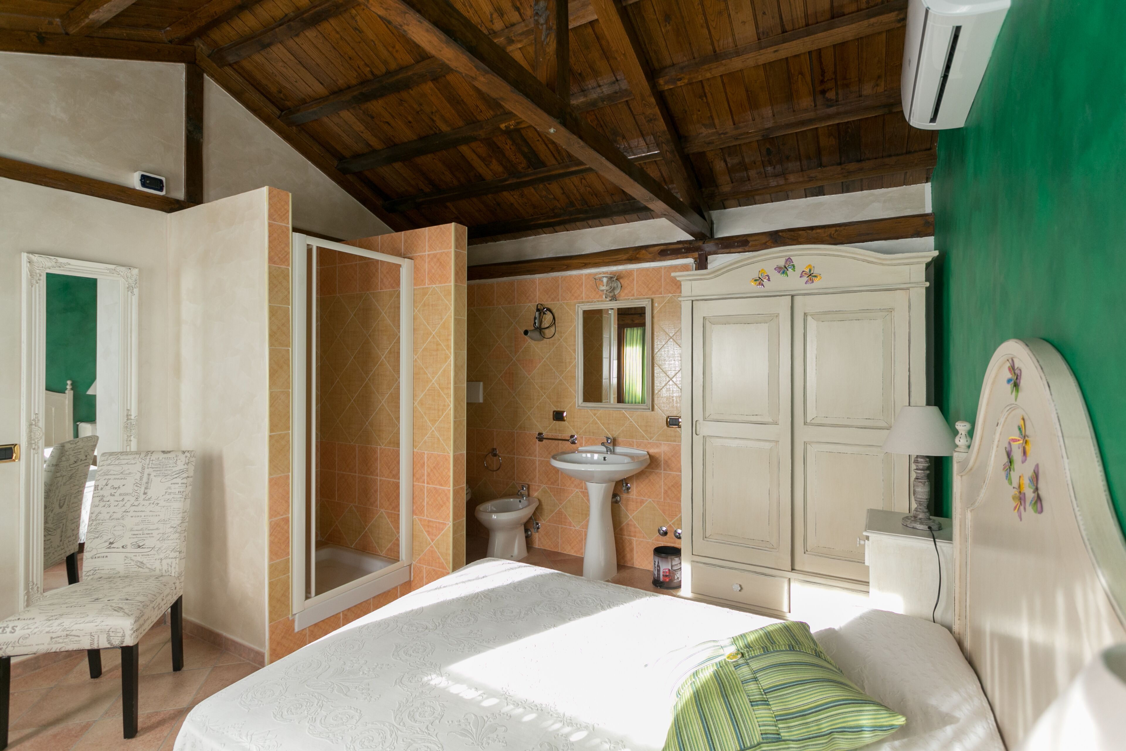 Ein Schlafzimmer mit Bett, Sessel, Bad mit Waschbecken und Spiegel sowie einem Kleiderschrank.