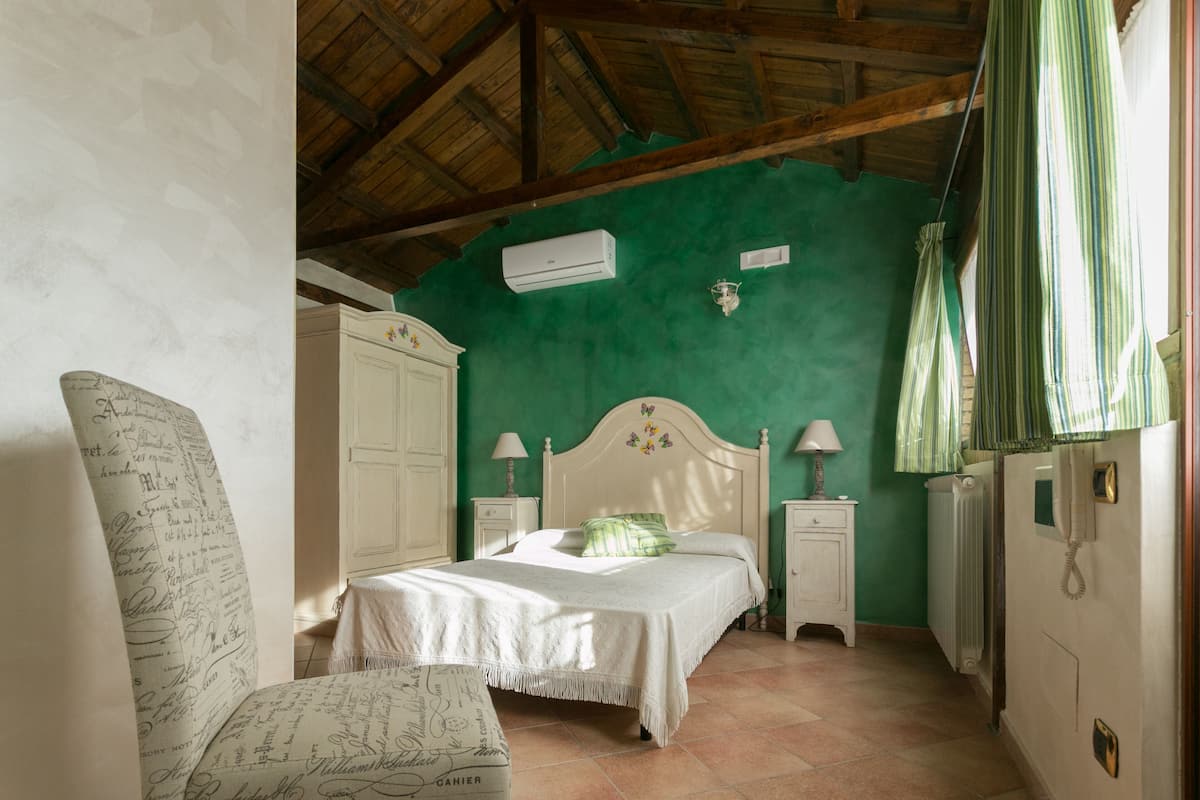A bedroom with a bed, a chair, a wardrobe, a nightstand, a lamp, and a radiator.