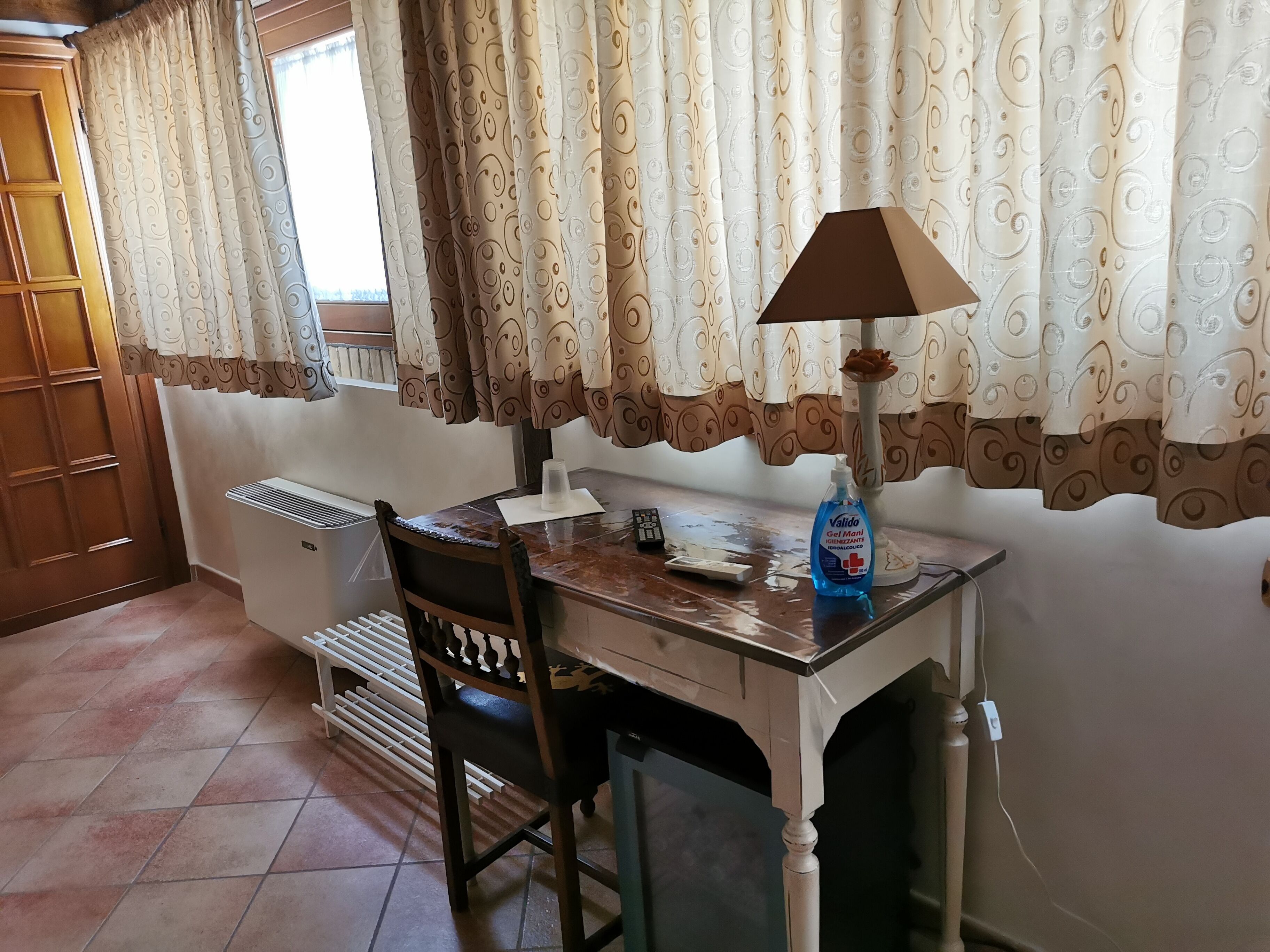 Een kamer met een houten bureau, een stoel, een radiator en een raam met gordijnen met een patroon.