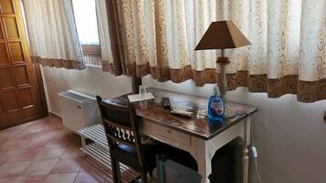 A room with a wooden desk, a chair, a radiator, and a window with patterned curtains.
