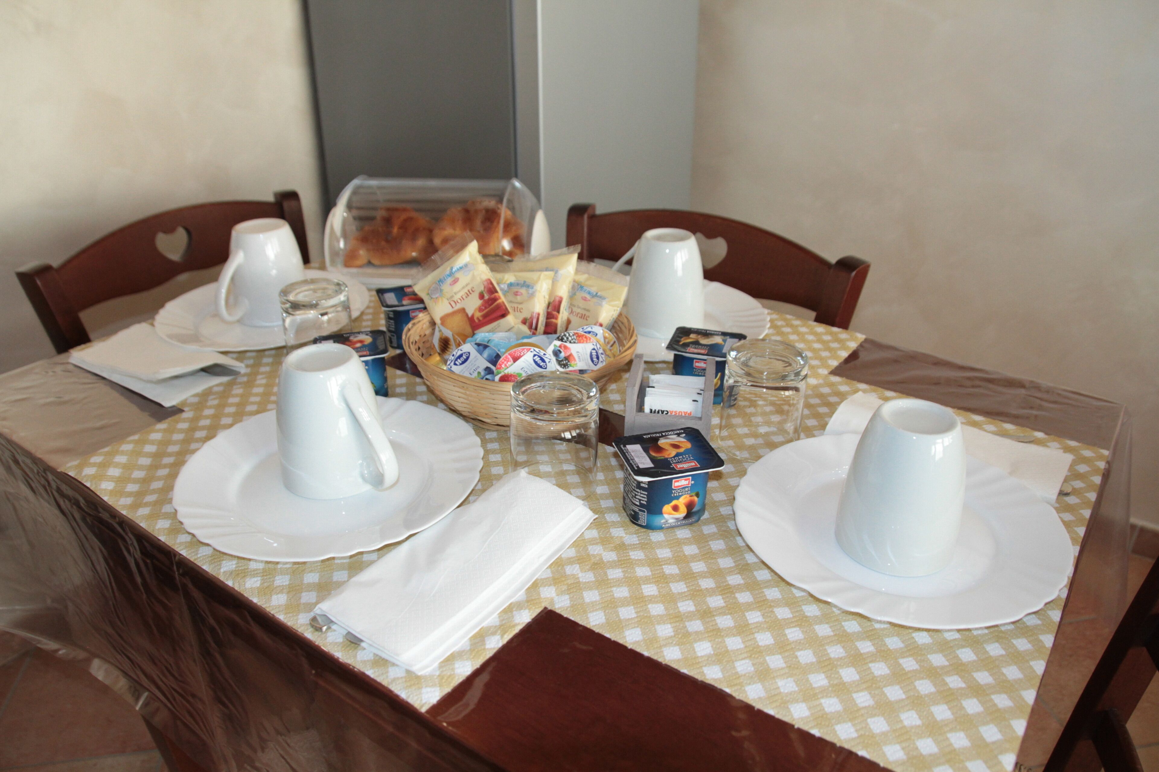 A breakfast table set with white plates, cups, and a basket of pastries.