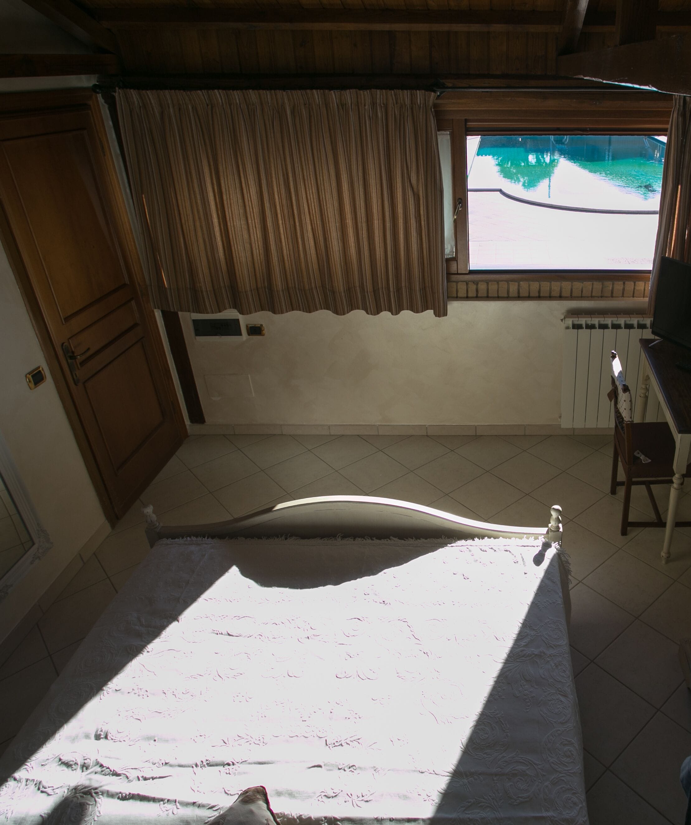 A bedroom with a bed, a window with curtains, a radiator, and a wooden door.