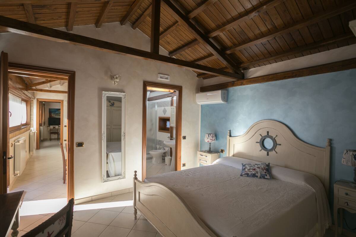 A bedroom with a wooden ceiling, a bed with a decorative headboard, a nightstand, and a mirror.