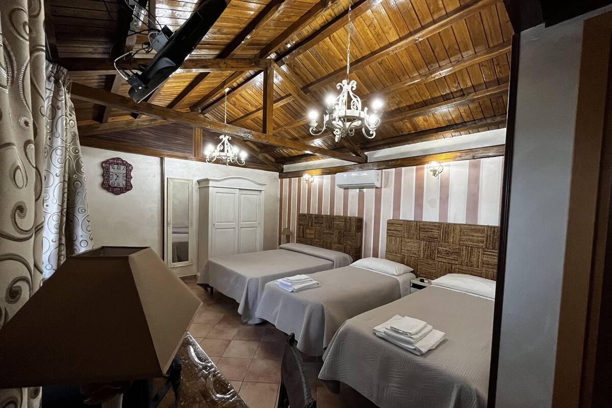 A room with two beds, wooden ceiling beams, a chandelier, and a clock on the wall.