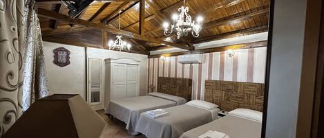 A room with two beds, wooden ceiling beams, a chandelier, and a clock on the wall.