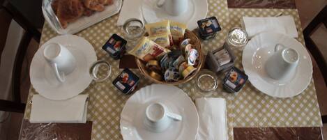A breakfast table set with plates, cups, and a basket of pastries.