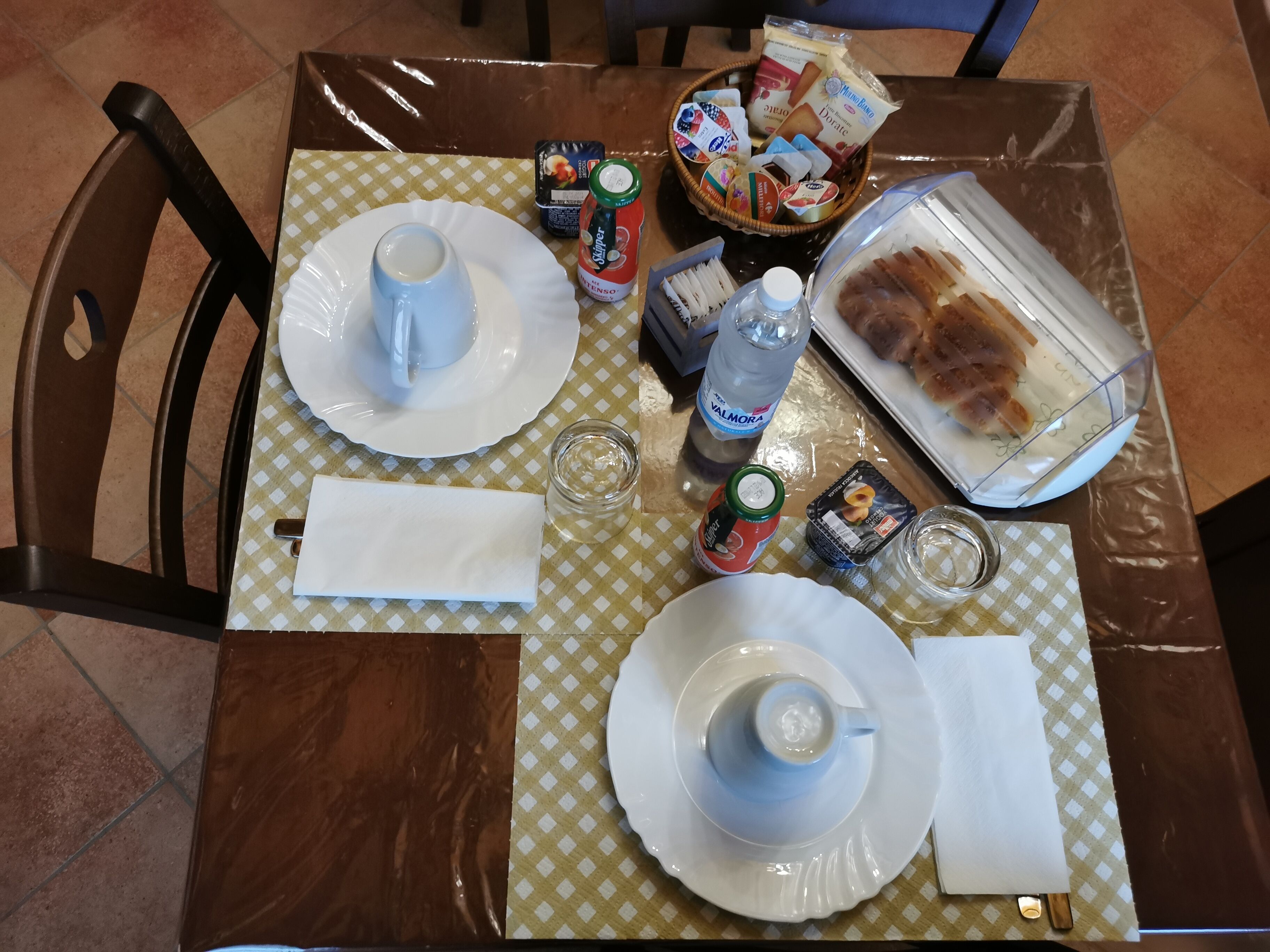 Une table à manger dressée avec des assiettes, des tasses, une bouteille et un plateau de nourriture.