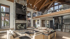 A spacious living area with a stone fireplace, a large sofa set, and a wooden staircase. - Newly Built | Ski-in/Ski-out | Hot Tub (Big Sky)