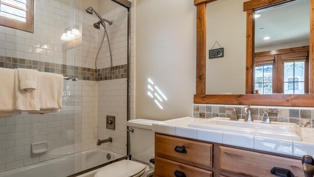 Een badkamer met een douchecabine van glas, een bad, een toilet en houten kastjes.