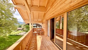 A wooden deck with a glass door leading to a balcony overlooking a lush garden and a mountain. - Ferienwohnung Mia, 100m², 2 Schlafzimmer, Wlan (Siegsdorf)