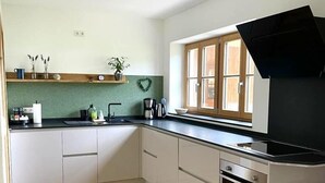 Cocina con armarios blancos, encimera negra, horno empotrado y ventana con contraventanas de madera.