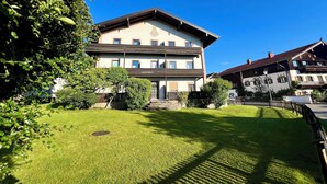 A two-story building with a balcony, surrounded by a well-maintained lawn and trees. - Ferienwohnung Almglück, Separates Schlafzimmer, Küche, Terrasse, TV, Wlan (Rottau)