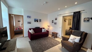 A living room with a red sofa, a brown armchair, a small table, and a TV on a wooden stand. - Ferienwohnung Almglück, Separates Schlafzimmer, Küche, Terrasse, TV, Wlan (Rottau)