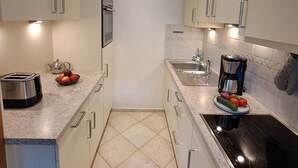 A modern kitchen with white cabinets, a stainless steel toaster, a kettle, a coffee maker, and a sink. - Ferienwohnung Almglück, Separates Schlafzimmer, Küche, Terrasse, TV, Wlan (Rottau)