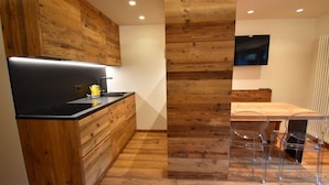 A modern kitchen with wooden cabinetry, a black countertop, and a built-in stove. There is a dining area with a wooden table and clear chairs.