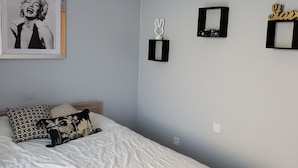 Un dormitorio con cama, almohadas, un cuadro enmarcado, un espejo y adornos en la pared.