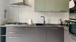 A modern kitchen with grey cabinets, a stainless steel range hood, a gas stove, a sink, and a built-in oven. - 5 minutes from the Valley of the Temples, apartment with free parking (Agrigento)