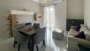 A modern living room with a dining table, houndstooth chairs, a sofa, a TV, and a ceiling light. - 5 minutes from the Valley of the Temples, apartment with free parking (Agrigento)