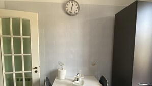 A kitchen with a white table, two chairs, a clock on the wall, a refrigerator, and a door with frosted glass panels. - 5 minutes from the Valley of the Temples, apartment with free parking (Agrigento)