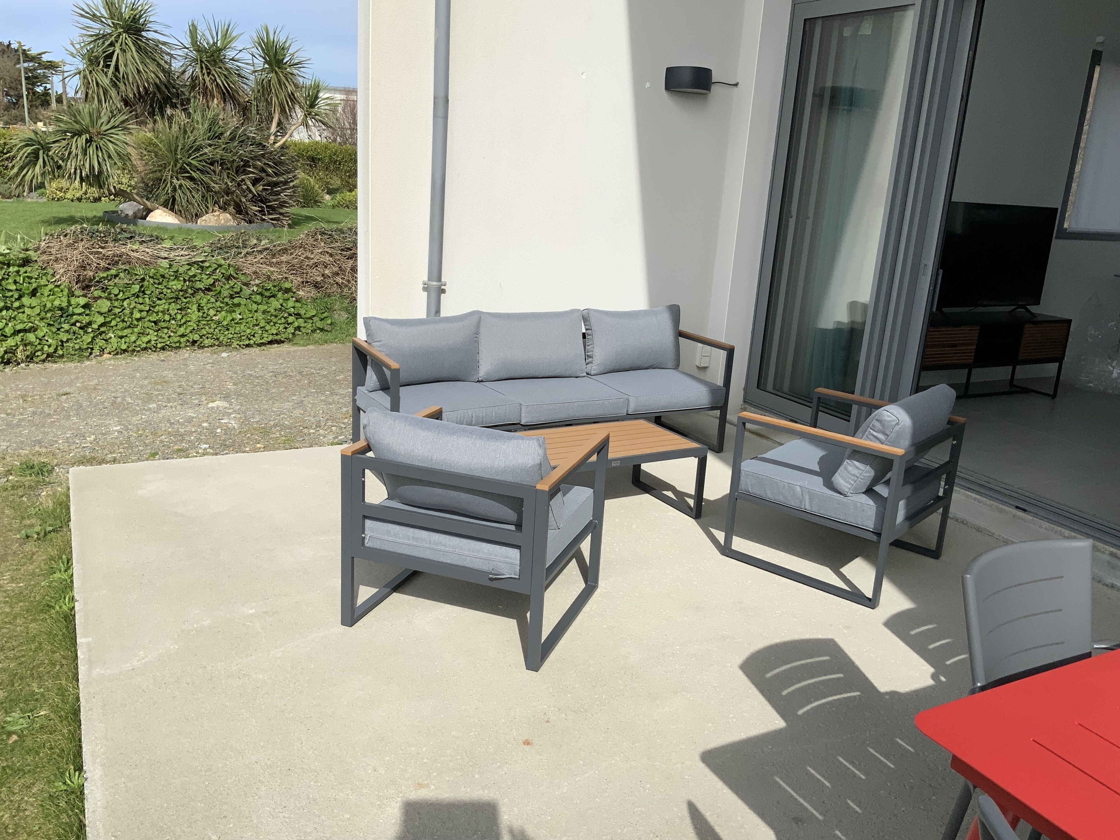 Un patio al aire libre con un sofá gris, dos sillones y una pequeña mesa de madera.