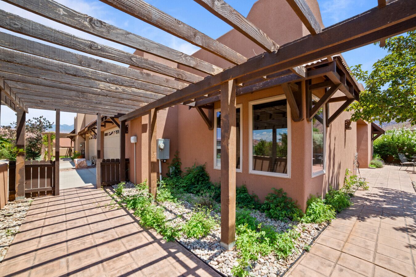 A covered outdoor area with a pergola, a patio with stone tiles, and a building with large windows. - Red Rock Oasis I Large Patio I Pool & Hot Tub I Views (Moab)