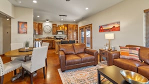 A spacious living area with a brown leather sofa, a dining table with chairs, and a kitchen in the background. - Red Rock Oasis I Large Patio I Pool & Hot Tub I Views (Moab)