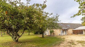 Ein rustikales Haus mit einem großen Baum im Hof, einem unbefestigten Weg und einer kleinen Sitzgelegenheit im Freien.