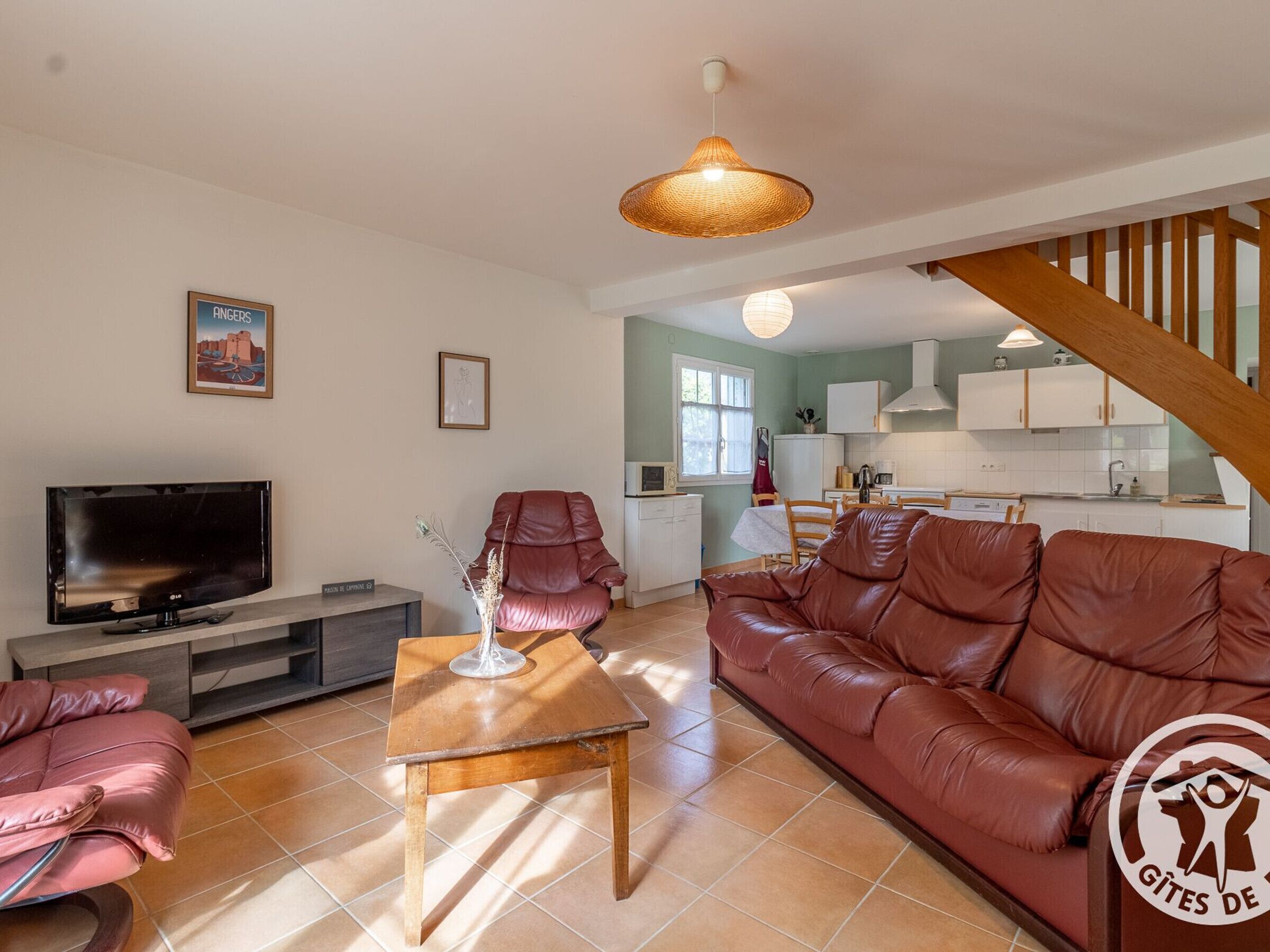 Una sala de estar moderna con un sofá de cuero, un televisor y un comedor con una cocina al fondo.