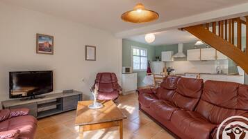 Una sala de estar moderna con un sofá de cuero, un televisor y un comedor con una cocina al fondo.