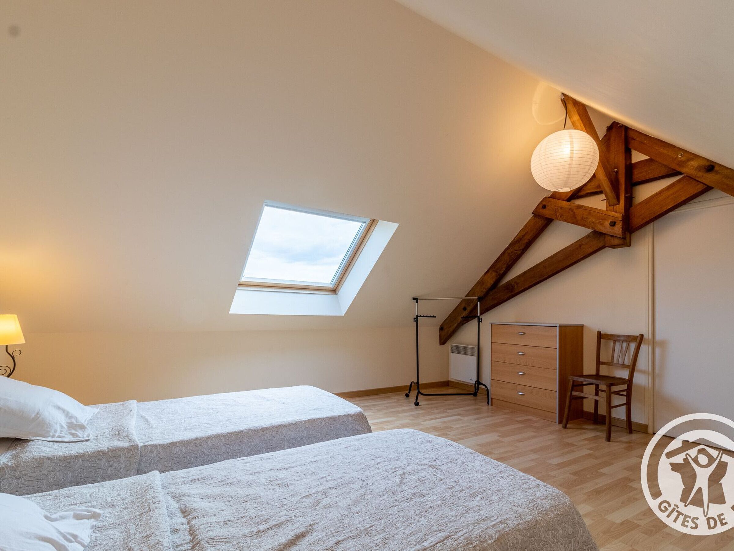 A bedroom with two beds, a skylight, a wooden ceiling, a desk, and a chair.