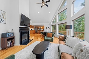 A spacious living room with a fireplace, a television, and a balcony with a view of trees. - HOT TUB! PRIME LEAF PEEPING! Gorgeous 4BR (Front Royal)