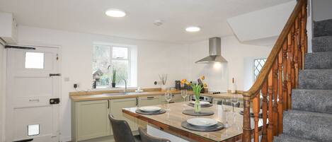 A modern kitchen with a central island, wooden bar stools, a built-in oven, and a staircase with wooden balusters.