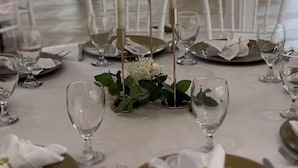 Un salón de banquetes con mesas redondas dispuestas para un evento formal, con manteles blancos, platos con borde dorado y centros de mesa con velas.