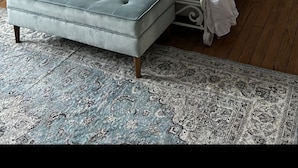 Une chambre à coucher avec un lit blanc à baldaquin, un pouf capitonné, un lustre et un tapis à motifs.