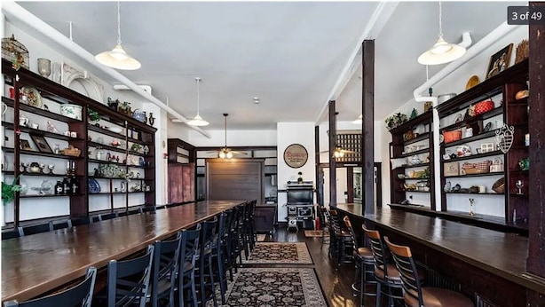 Un comedor amplio con mesas y sillas de madera alta, rodeado de estanterías llenas de objetos decorativos.