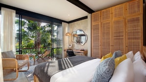 A spacious bedroom with a large bed, a desk, and a chair, a balcony with a view of palm trees, and a large mirror on the wall.