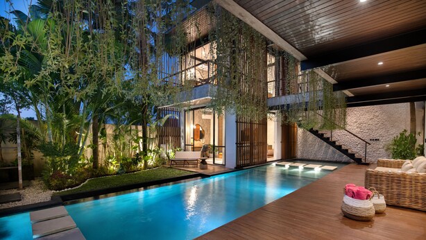 A modern pool area with a wooden deck, stone steps, and a staircase leading to a second level.