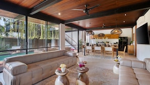 A spacious living area with a large sofa, two wooden coffee tables, and a dining area in the background.