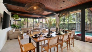 A spacious living area with a wooden ceiling, large windows, and a dining table set for six.