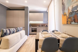 Una sala de estar moderna con un sofá, una mesa de comedor preparada para cuatro comensales y una cocina al fondo.
